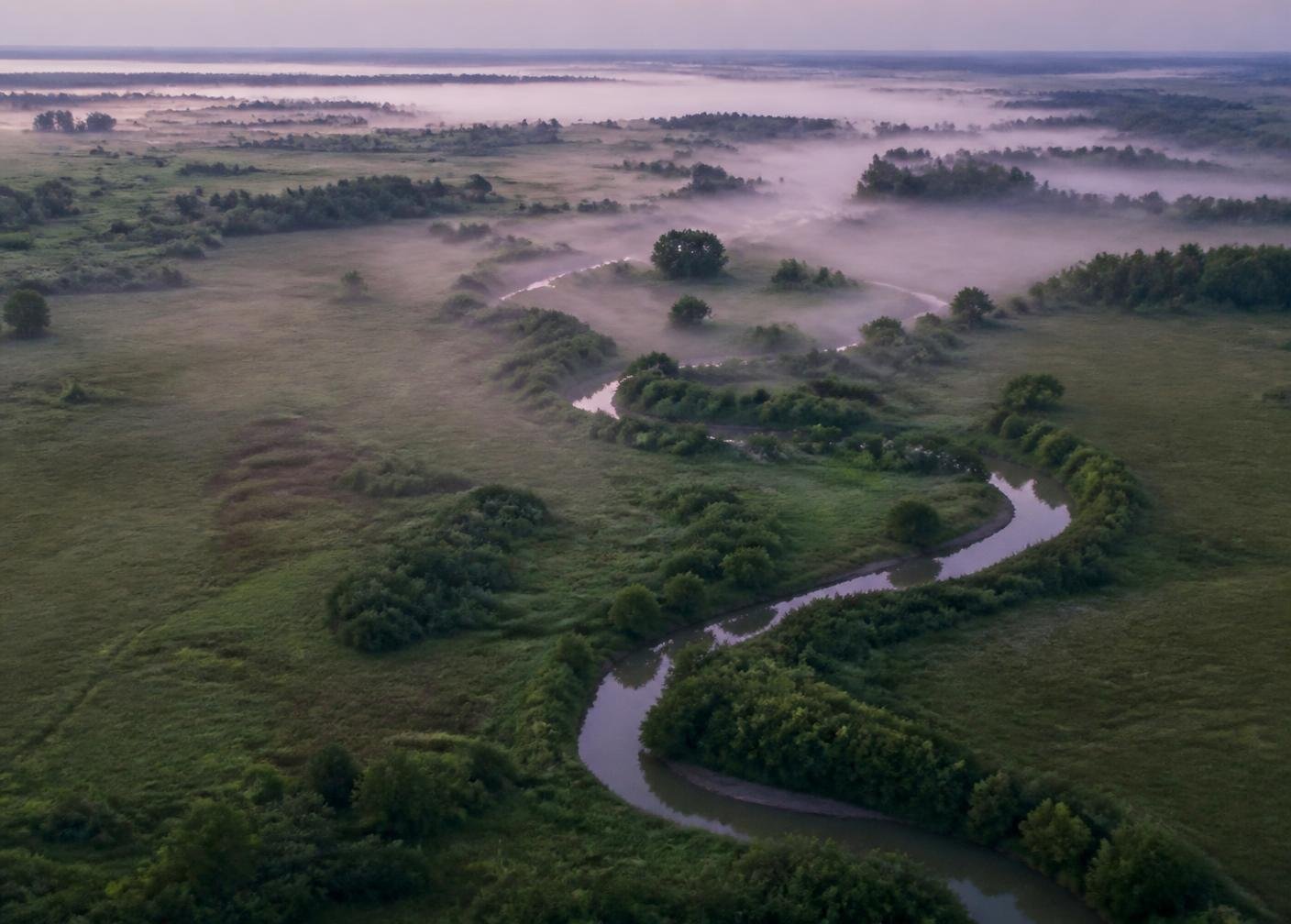 Aerial view of a winding creek through green rural acreage